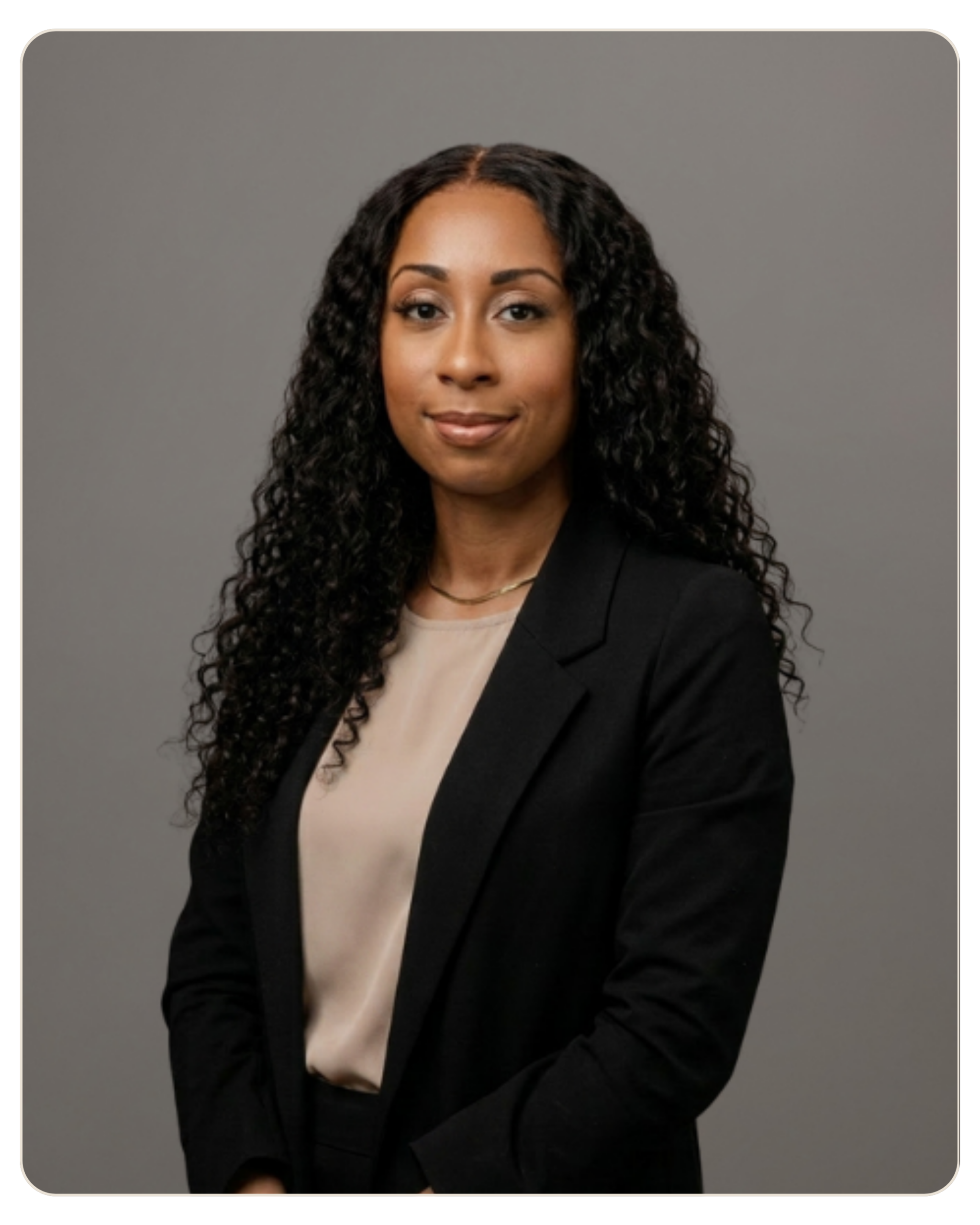 Flyland - Trost - Alexanderia Van Dyke, MA Professional headshot of a woman with long curly hair, wearing a beige blouse and black blazer against a gray backdrop for a corporate portrait.