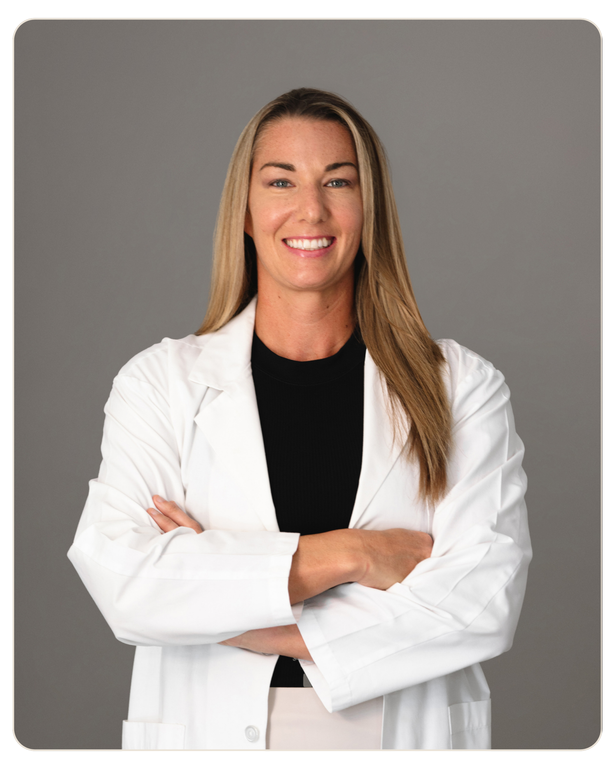 Dr. Pamela Tambini Medical Director Smiling woman in a white lab coat with arms crossed against a gray backdrop.