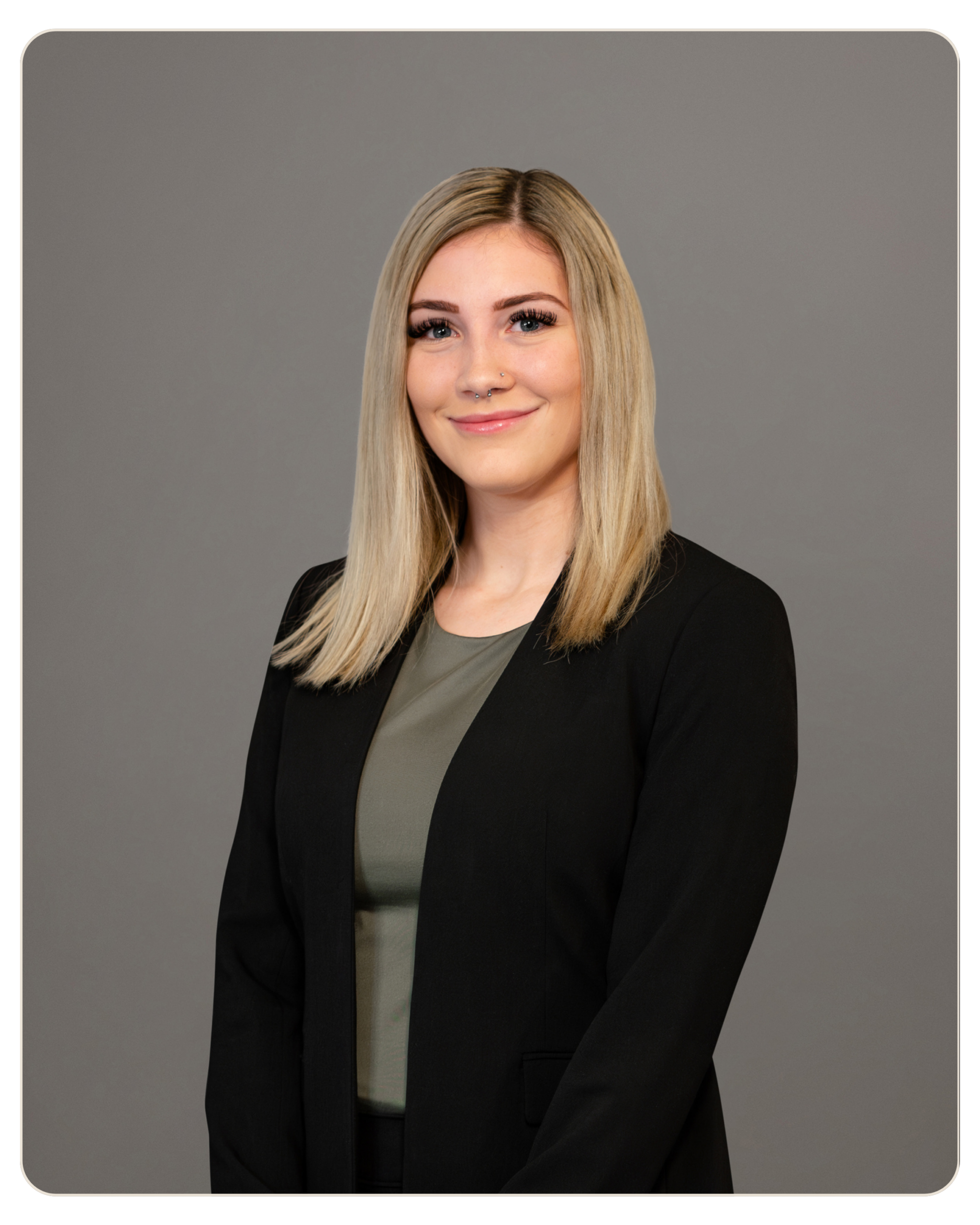 Nicole Laska Trost Smiling head-and-shoulders portrait of a professional woman with blonde hair wearing a black blazer against a gray backdrop