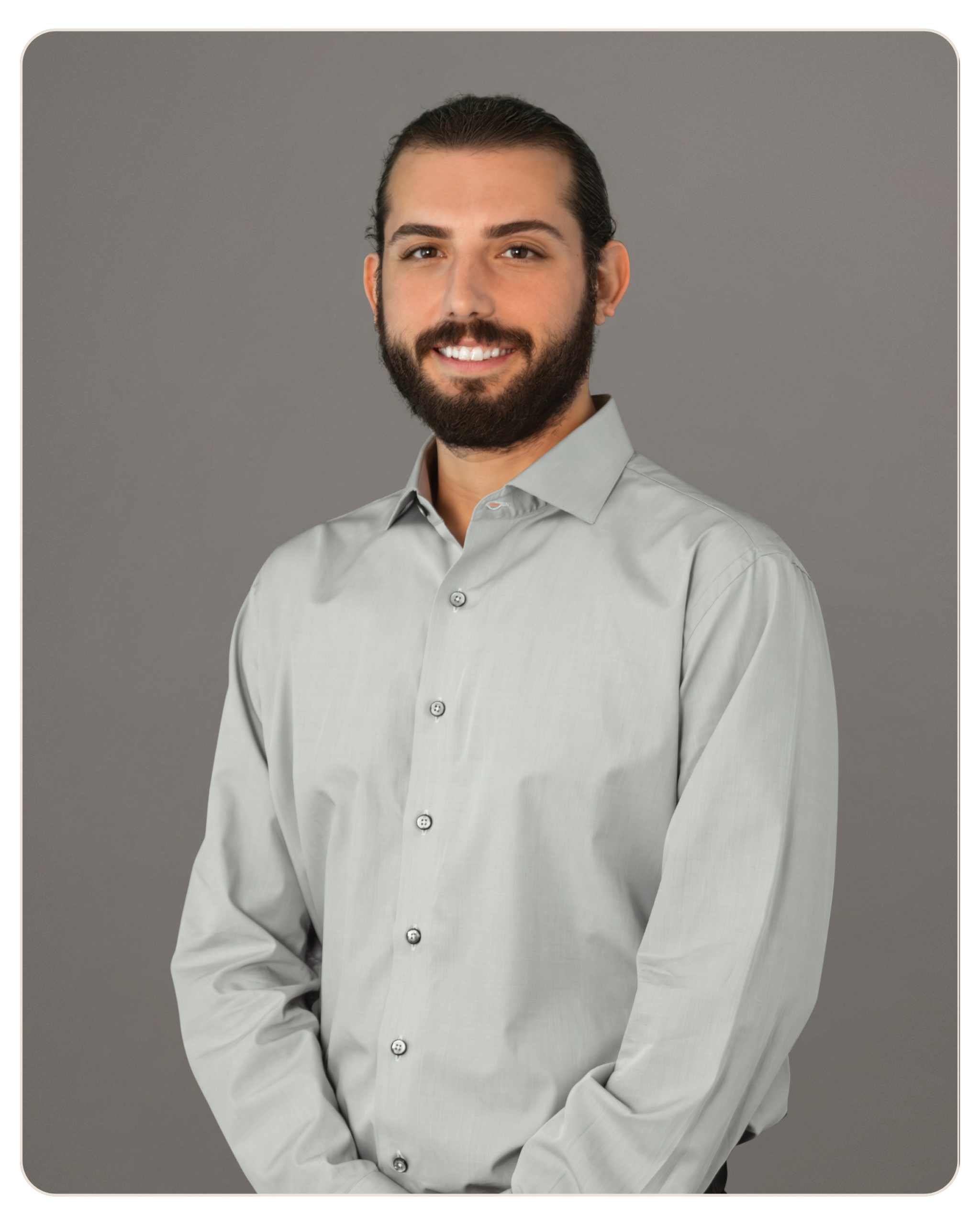 Flyland - Trost - Robert Mazo Smiling man with dark hair and beard in a light gray button-down shirt against a gray studio backdrop